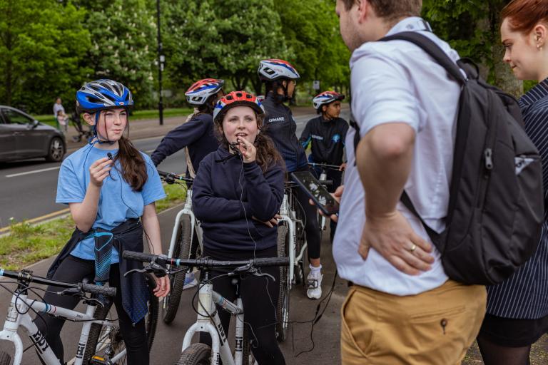 Teenagers stood on their cycle talking to adults