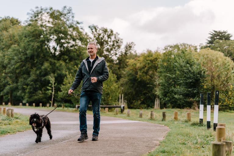 Older man walking dog in park, unknown location