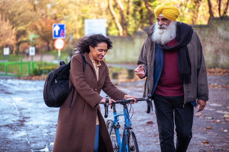 Man and woman walking, the woman has a cycle, unknown location