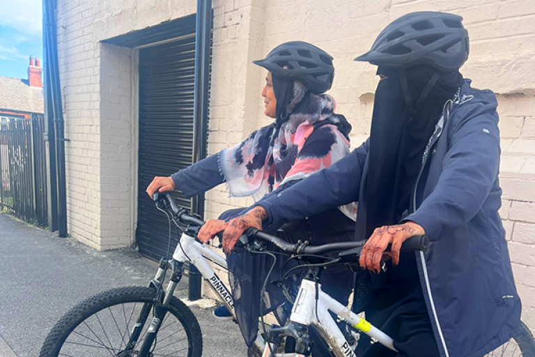 Two women pose on bicycles