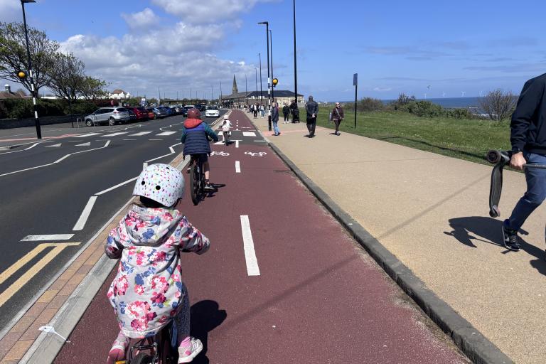 Children cycling along a cycle path next to a road.