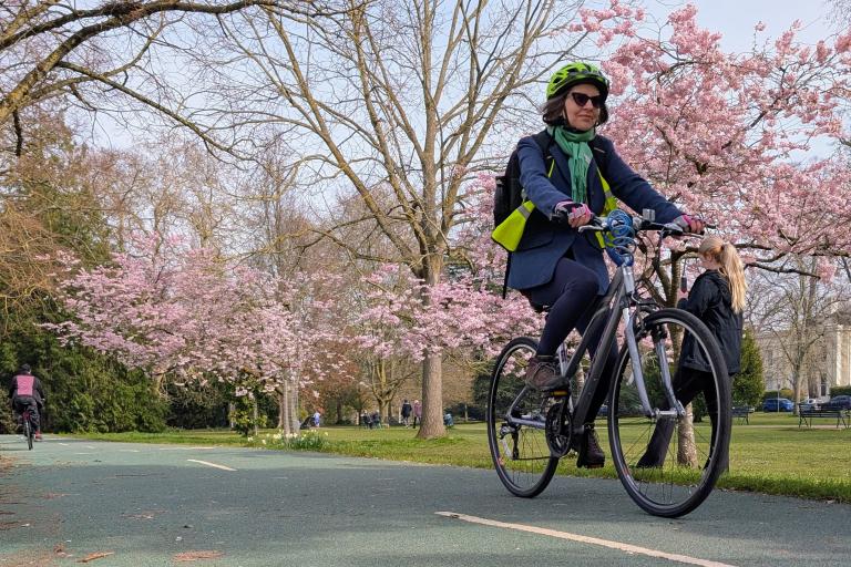 A person cycles along a cycle path. In the background are trees.