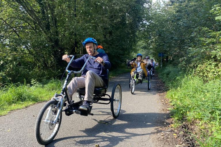  People riding adapted trikes on a wide path in a rural setting